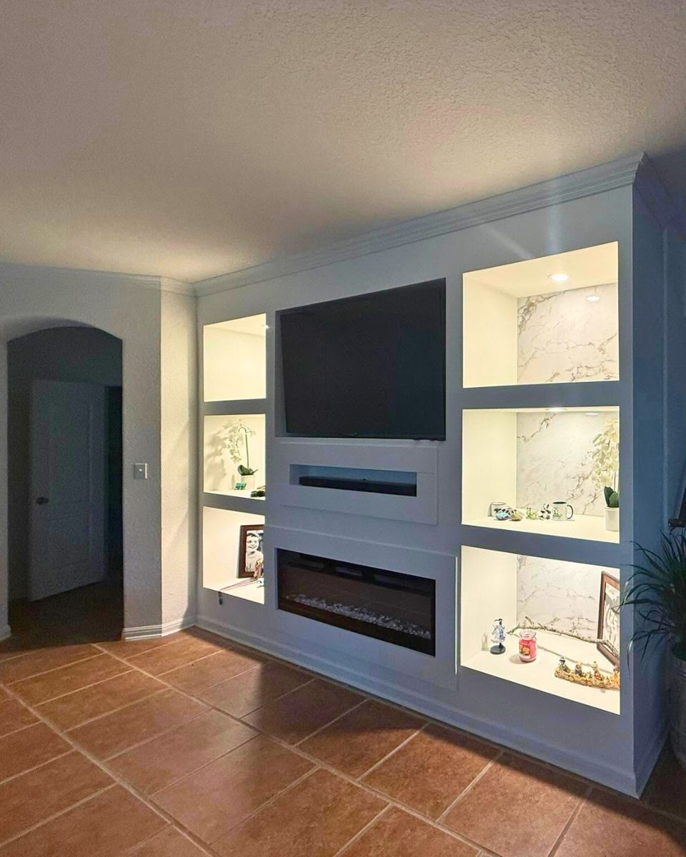 Custom built-in media wall with mounted TV, electric fireplace and lit display shelves