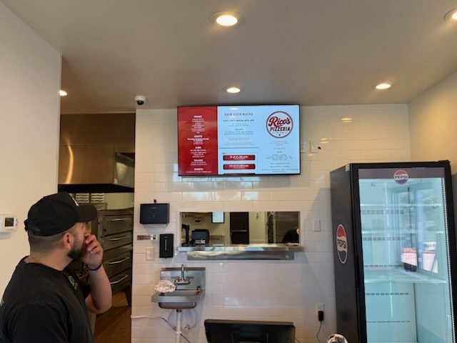 Digital menu board TVs mounted above a pizzeria counter